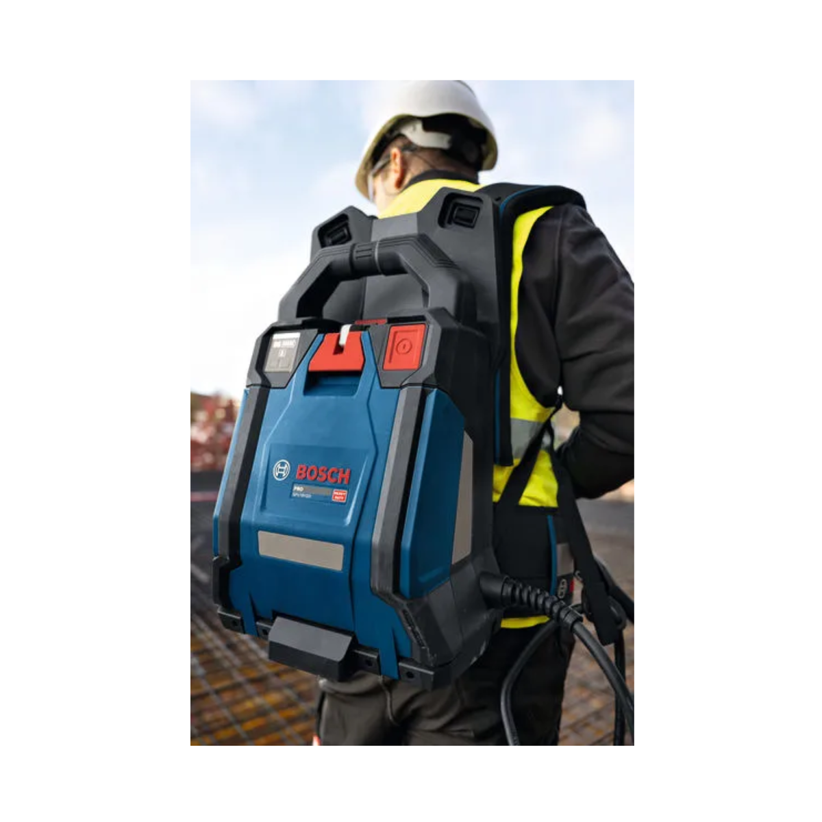 A worker viewed from behind wearing a Bosch backpack power tool, with the blue and black tool strapped on their back. The worker is wearing a white hard hat and a high-visibility yellow vest, set against an outdoor construction background.