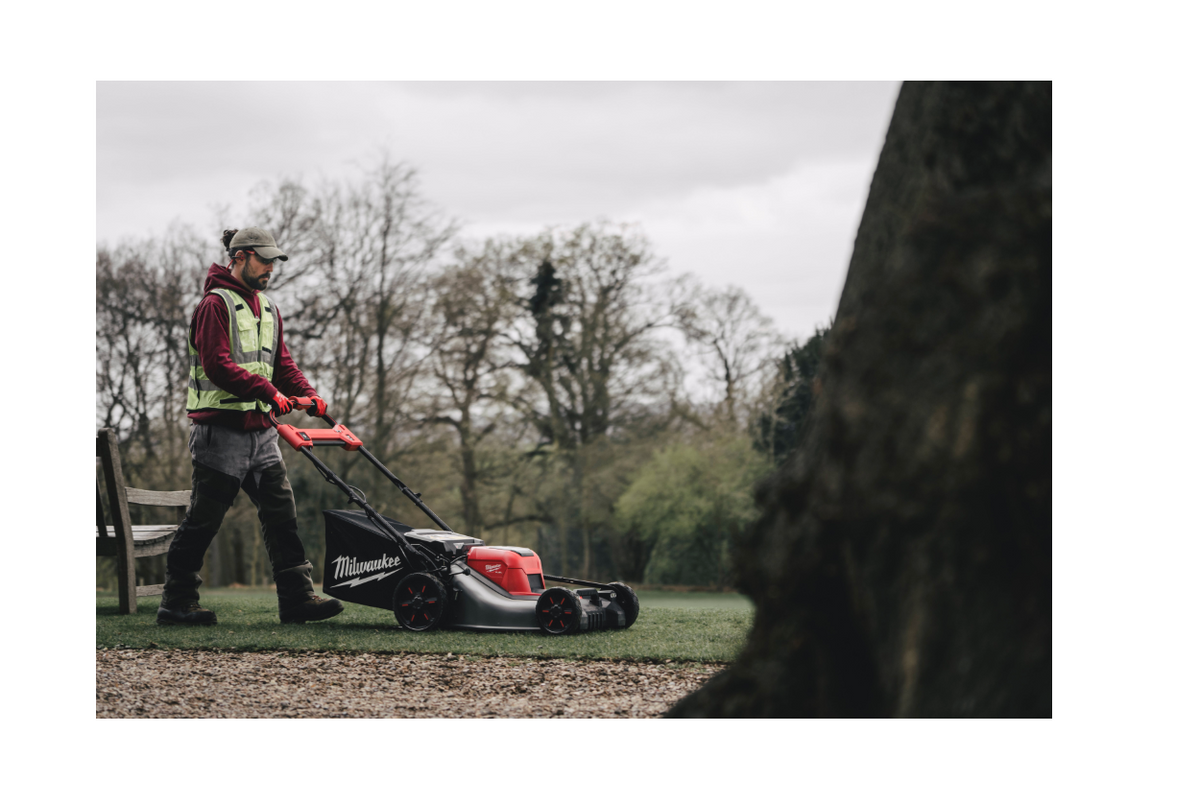 Person using a lawn mower in an outdoor setting with trees and grass.
