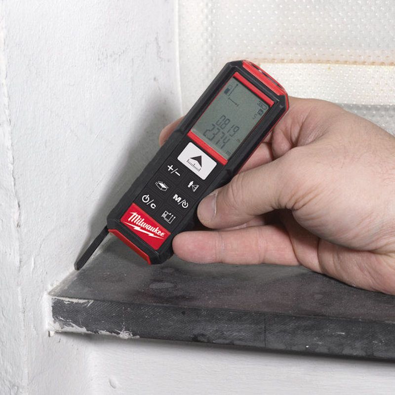 Hand using a Milwaukee stud finder on a wall.