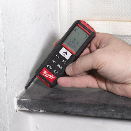 Hand using a Milwaukee stud finder on a wall.