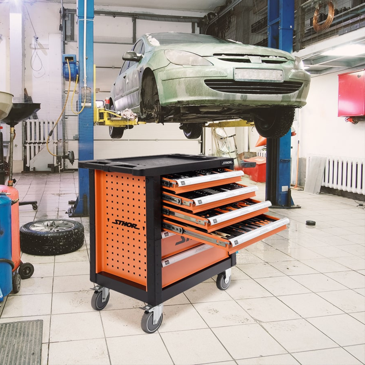 Orange tool cart with open drawers in a garage setting with a car on a lift.