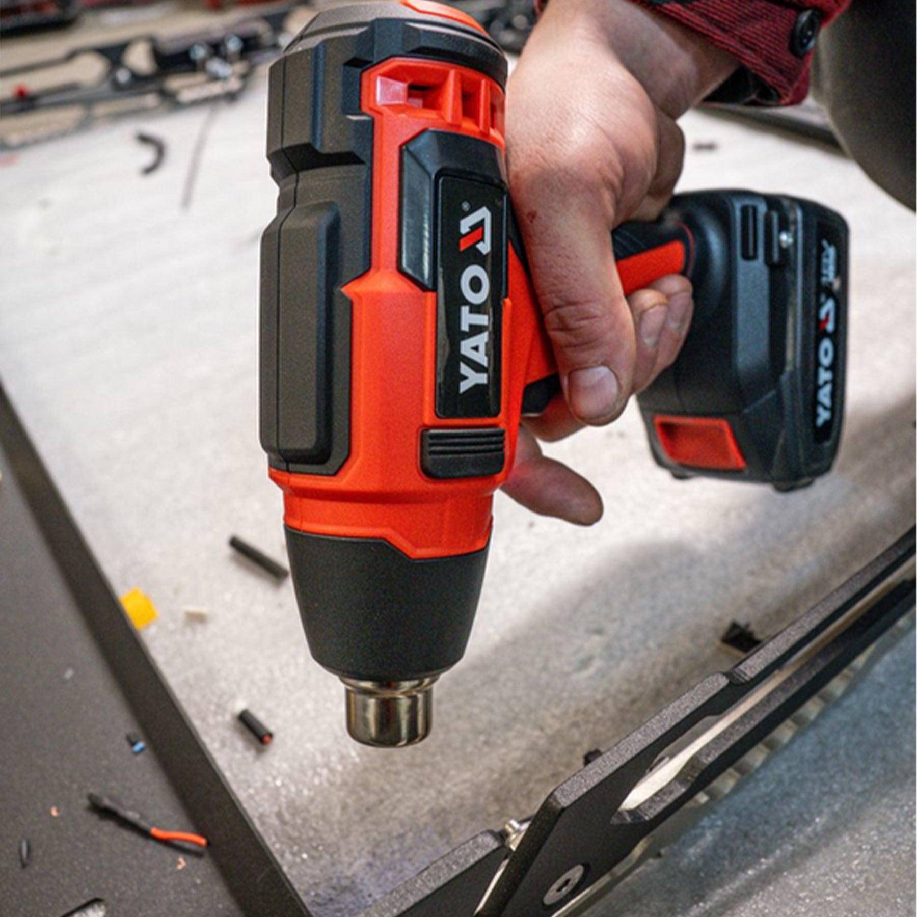 Hand holding a Yato cordless drill with battery pack on a workbench.