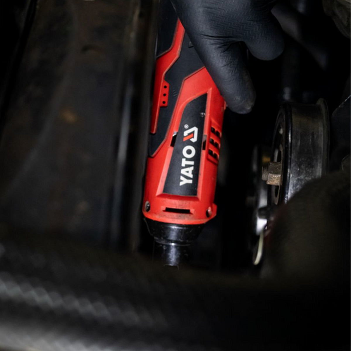 Red and black Yato tool being used on a vehicle component.