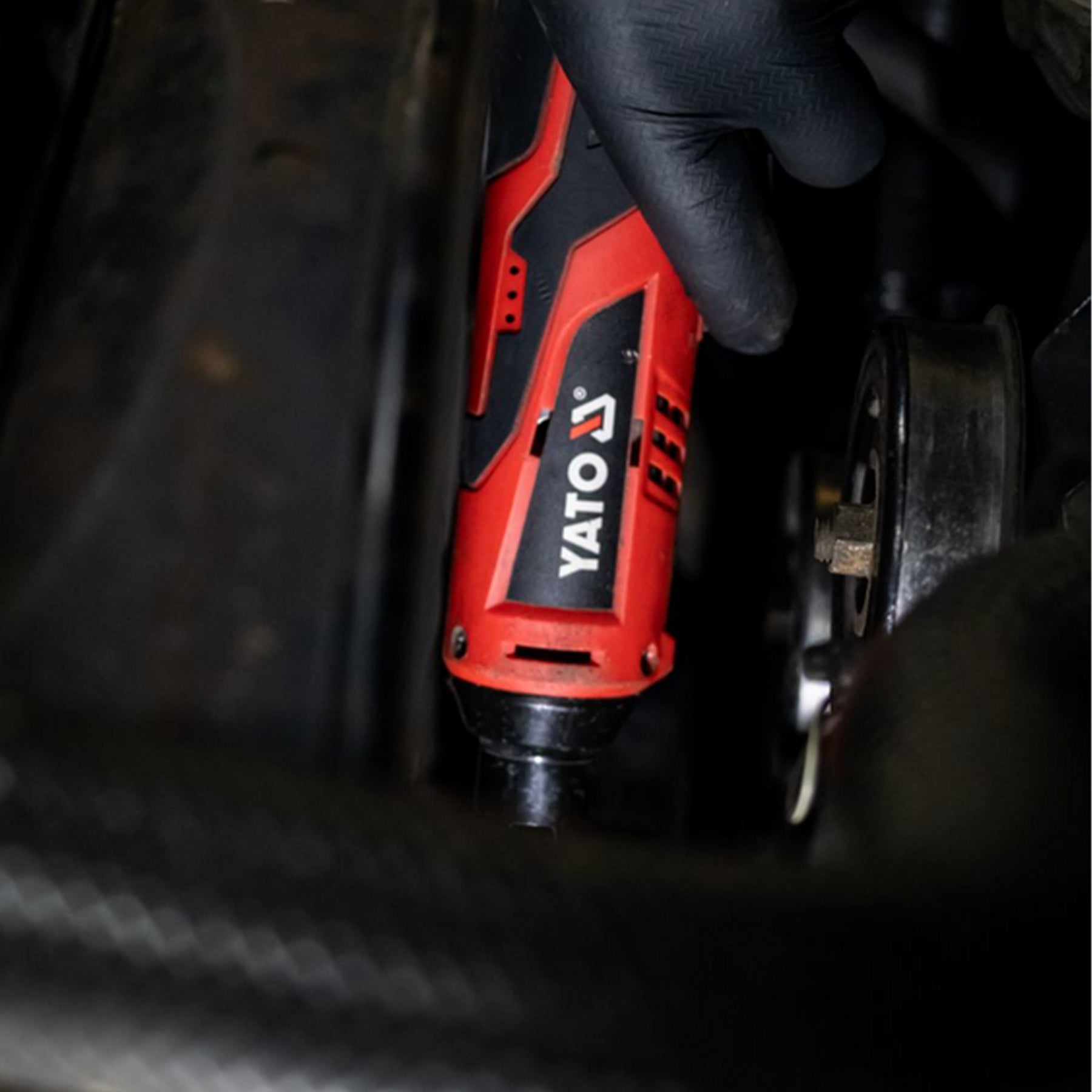 Red and black Yato tool being used on a vehicle component.