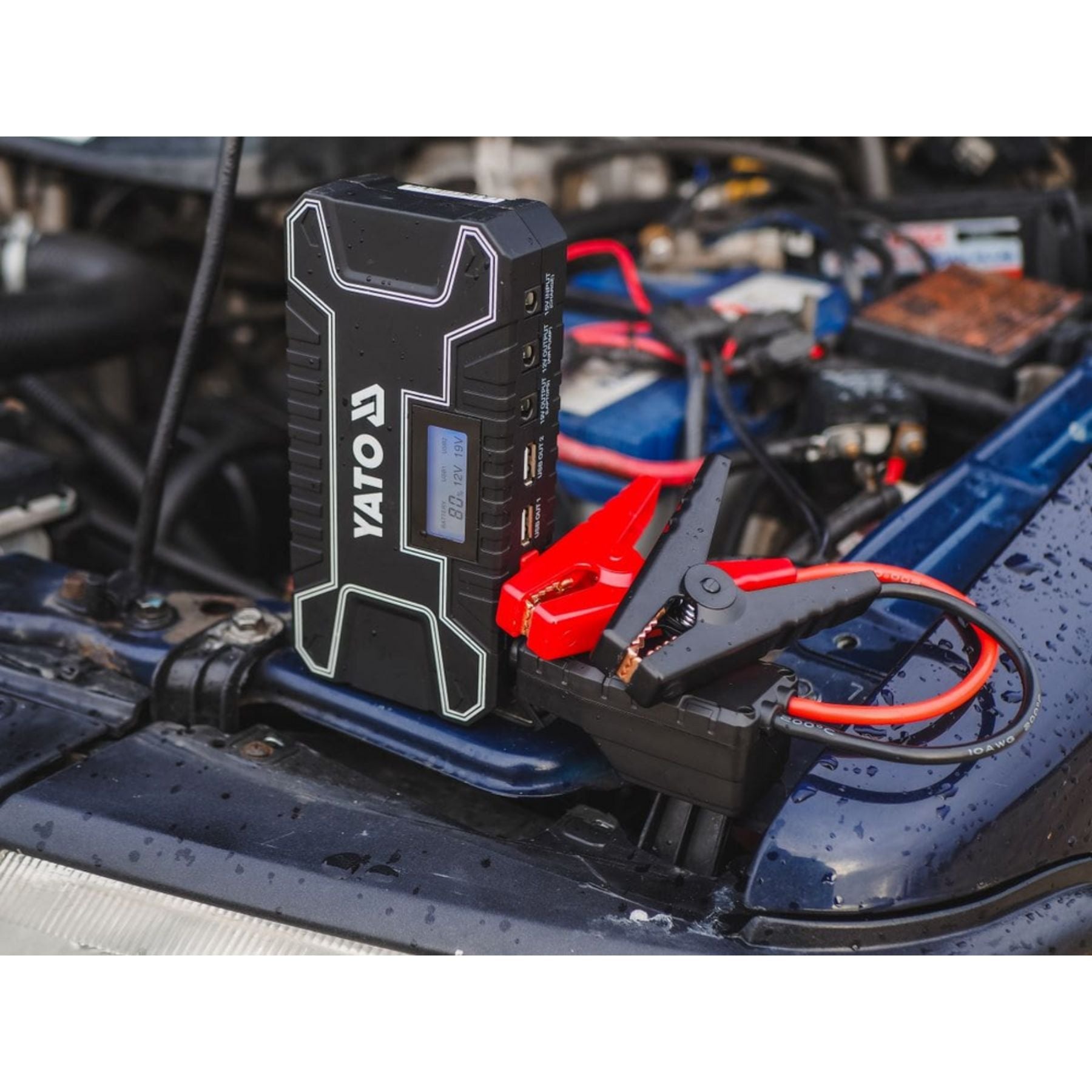 Yato jump starter device on a car battery with engine components in the background