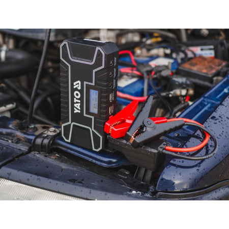 Yato jump starter device on a car battery with engine components in the background