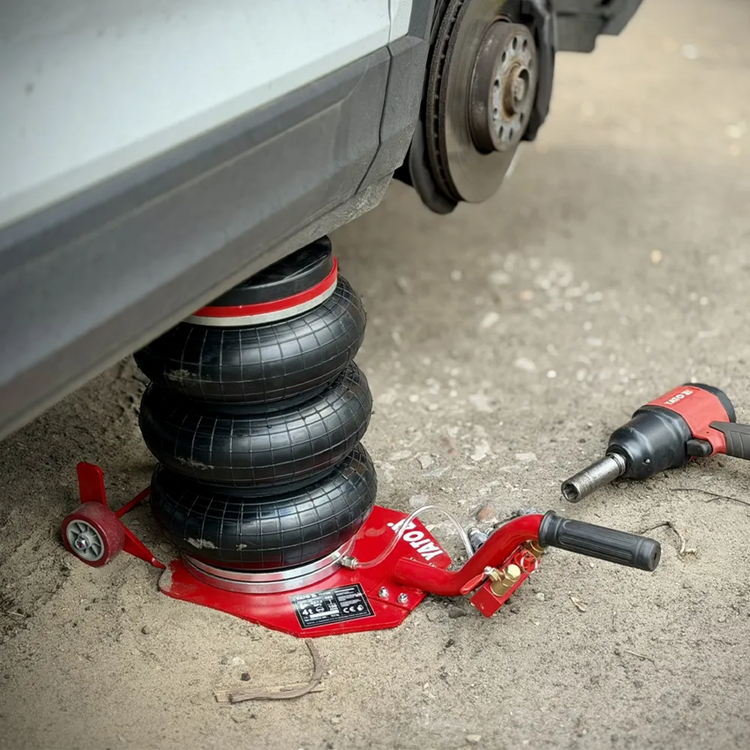 Red car jack supporting a vehicle with a tire on a concrete floor.