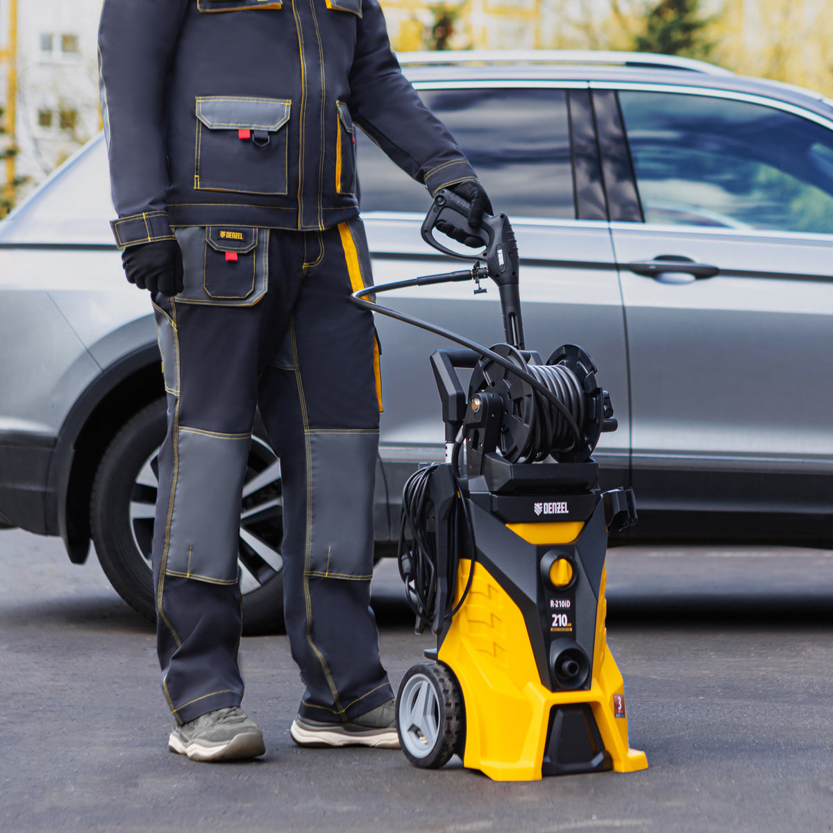 Person in work attire standing next to a yellow and black pressure washer in front of a car.
